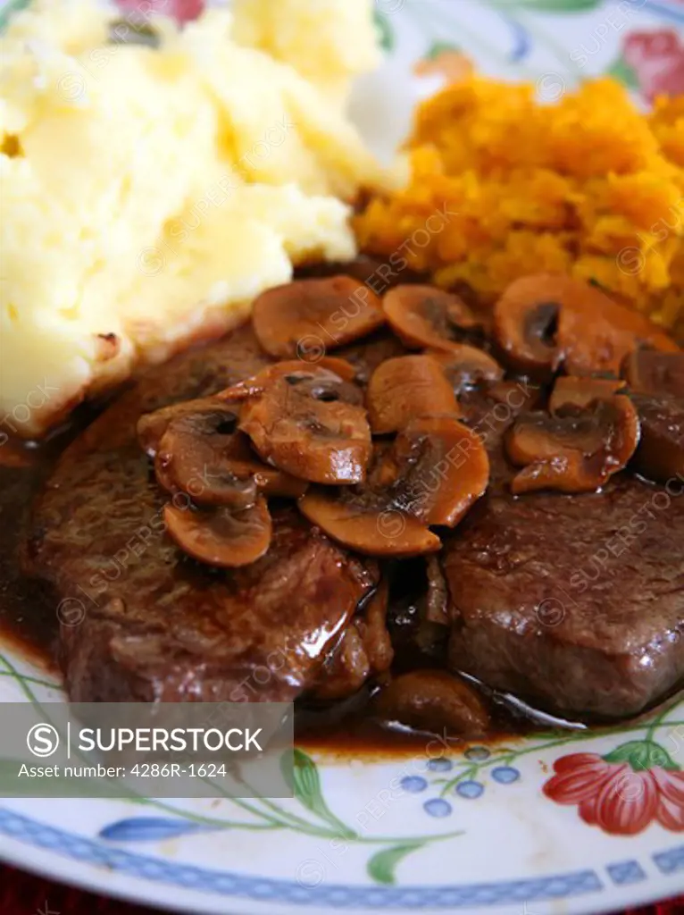 A meal of rump steak with mushrooms, gravy, mashed potatoes and garlic carrots.