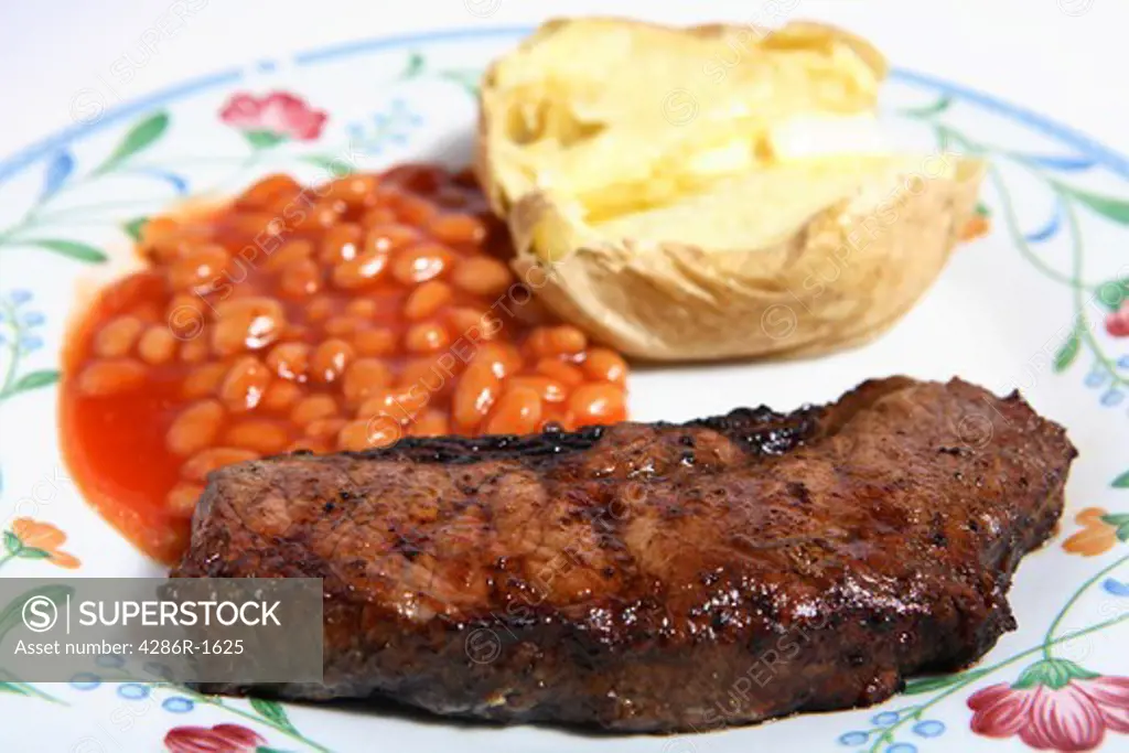 A barbecued sirloin steak served on a plate with baked beans in tomato sauce and a baked potato topped with butter.