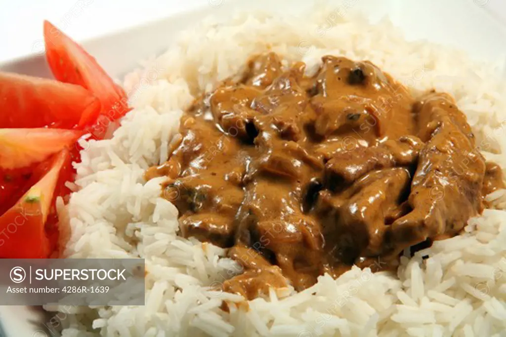Close-up on a plate of beef and mushroom stroganoff, on basmati rice garnished with tomato.