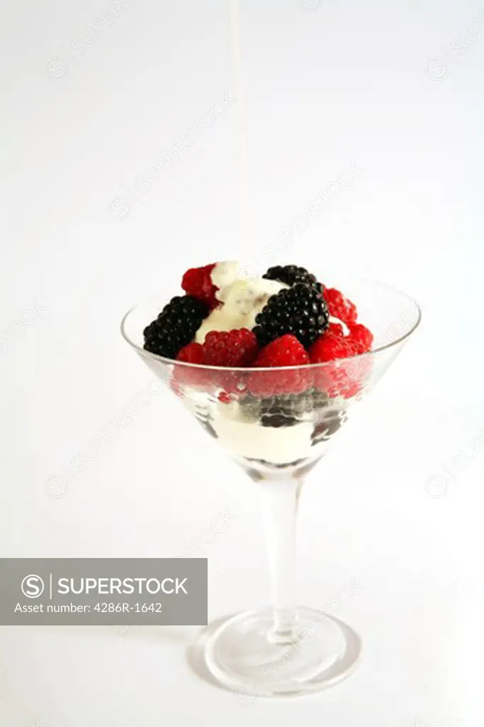 Blackberries and raspberries being drizzled with cream in a cocktail glass