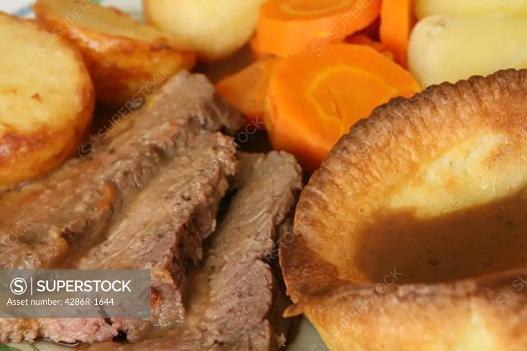 Extreme close-up on a dinner of roast beef and Yorkshire pudding, with roast and boiled potatoes and carrots.