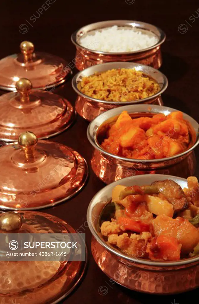 Bowls of curry and rice lined up. From the front, vegetable curry, Punjabi potato curry, coconut pilau rice and plain rice.