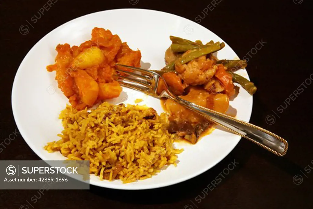 An Indian vegetarian meal: coconut pilau rice with vegetable curry and Punjabi potato curry on a dark wood table.