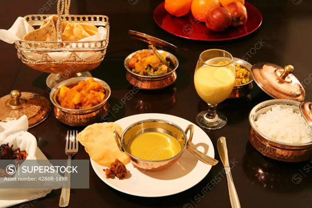 A meal of mulligatawny soup, white rice, coconut pilau rice, onion bhaji, poppadums, potato curry, veg curry, mango lassi and fresh fruit.