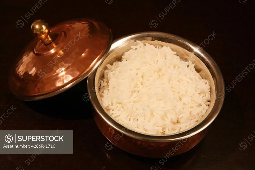 White basmati rice served in an authentic copper-clad Indian serving bowl, on a dark wood table.
