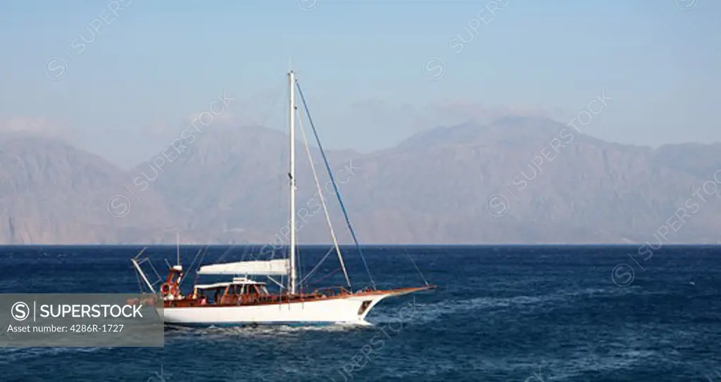 A pleasure yacht approaches Aghios Nikolaos harbour, Crete, with the cloud capped mountains of eastern Crete in the background.