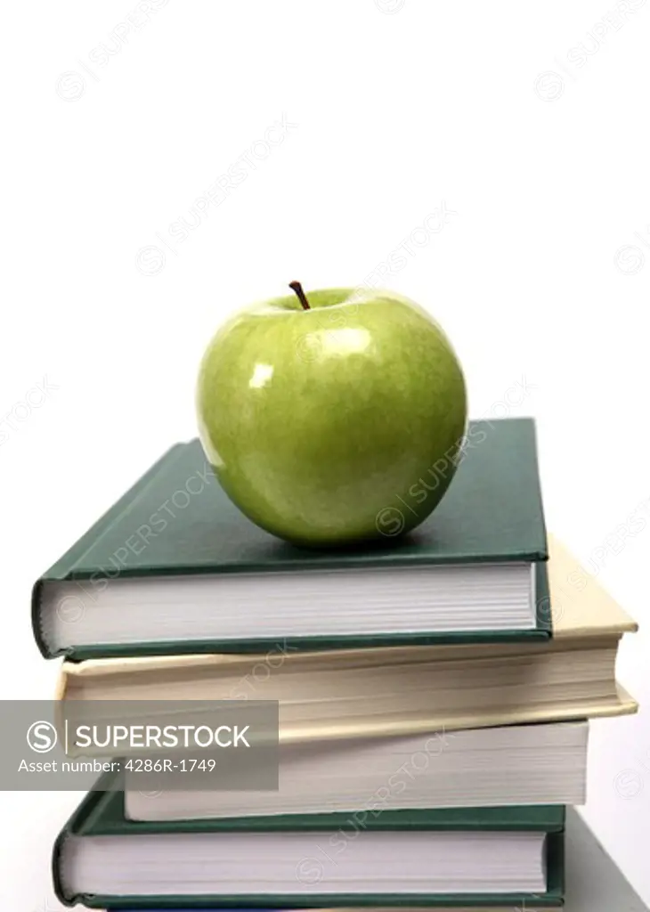 A shiny green apple on a pile of text books.