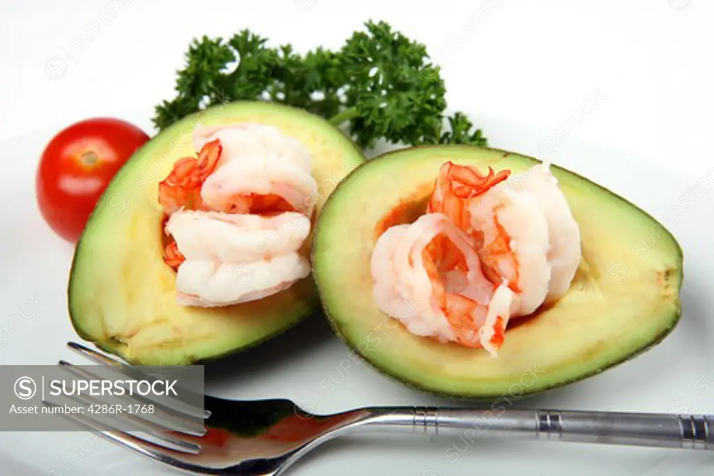 An avacado (guacamole) boat filled with prawns, served with a cherry tomato and parsley garnish