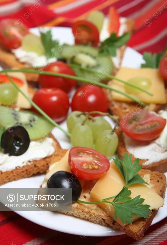 A plate of rusk or melba toast canapes, with cream or hard cheese and garnished with grapes, cherry tomatoes, capsicum slivers, parsley and chives.