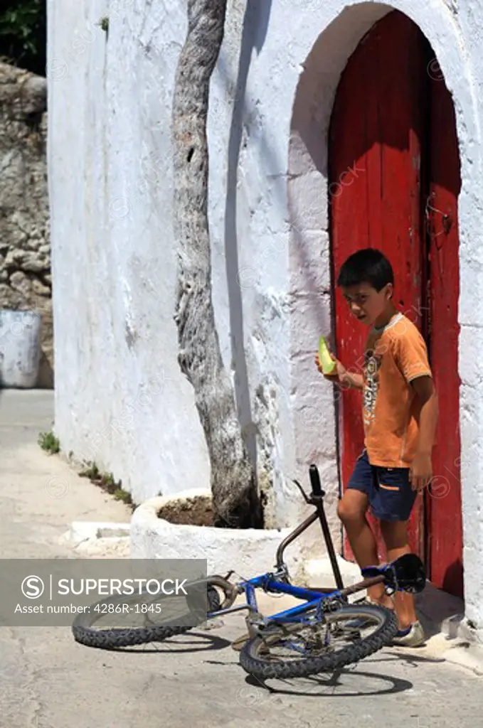 A boy leaves an old Greek village house in Prines, Rethymnon Praefecture, Crete, holding a slice of cantaloupe melon. Traditional ways of living still continue in the Cretan villages,