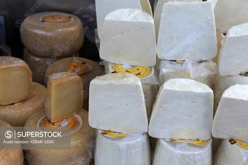 Traditional graviera and athotiri Cretan sheep or goat's milk cheeses on display at Rethymnon farmers' market. The maker's address is visible on some labels.