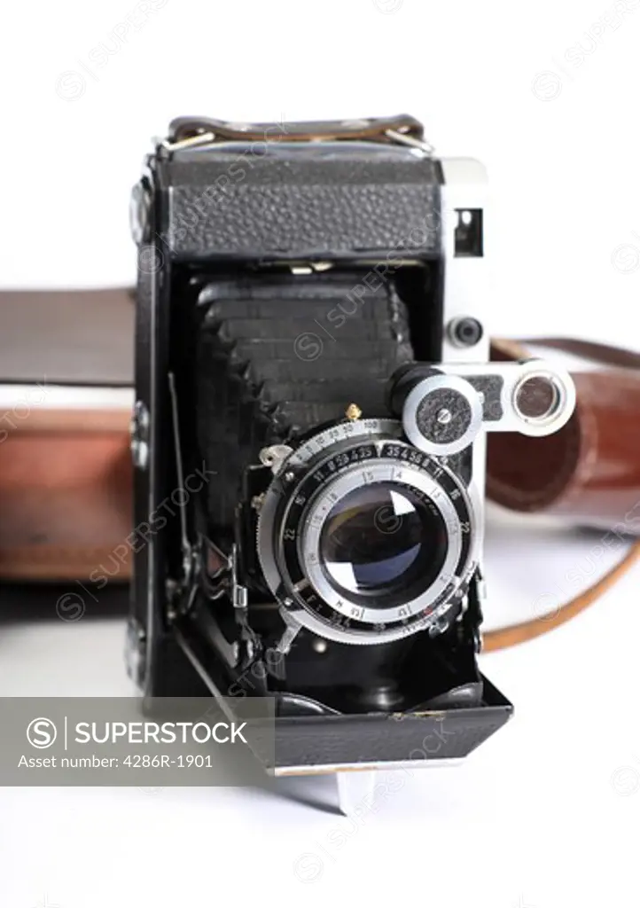 A rangefinder folding camera from the end of the 1950s, markings removed, with its leather case behind it.
