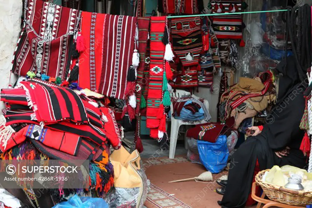 A Qatari woman (right) shrouded in her black abaya cloak, becomes almost invisible among the wares of her textile shop in Souq Waqif, Doha, Qatar.