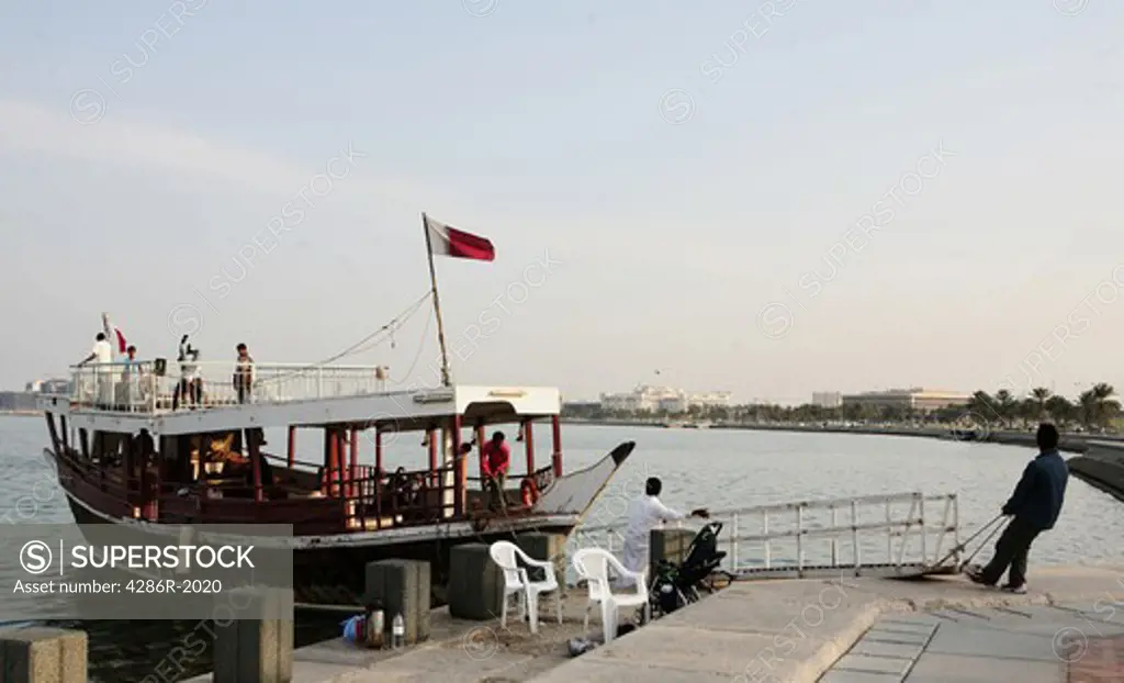 A pleasure dhow preparing to sail for a trip round Doha Bay, Qatar. The Emiri Diwan palace and other government buildings are in the background.