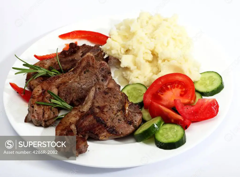 A meal of grilled lamb chops, mashed potato and tomato and cucumber salad