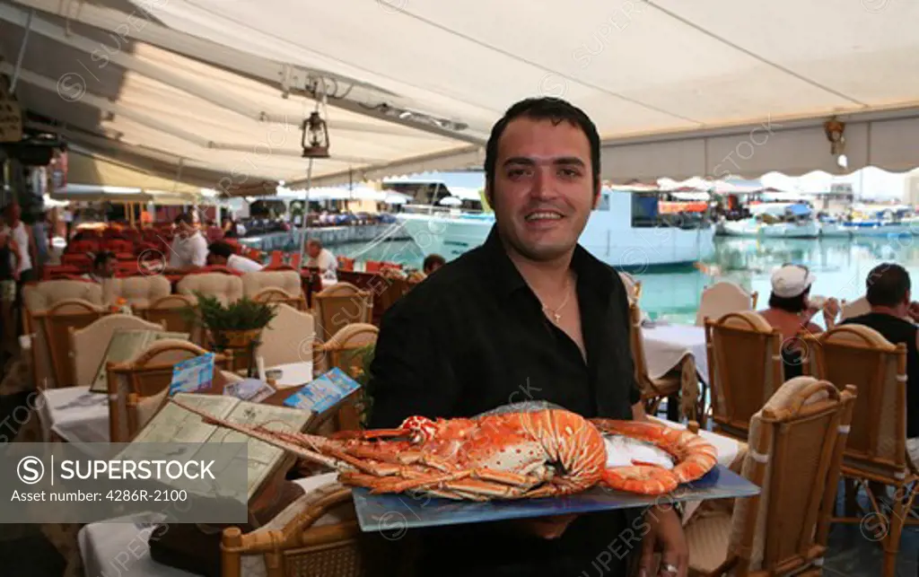 A waiter displaying a lobster at Helena fish taverna on the Venetian Harbour quay in Rethymnon, Crete, Greece