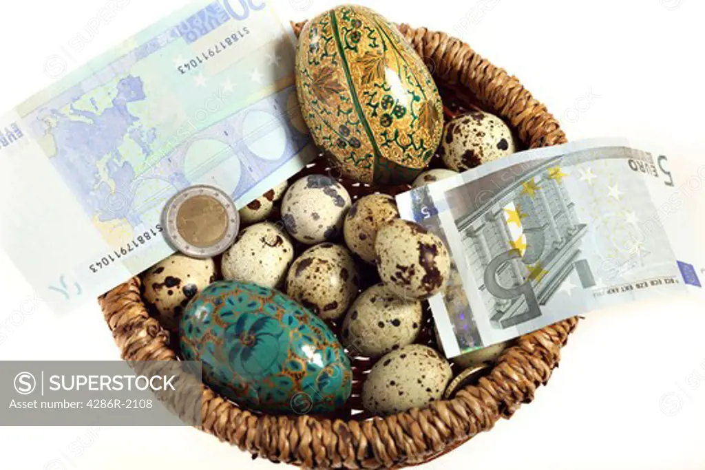 Looking down on a basket of eggs - quails and artificial - and euro currency notes and coins. A financial concept shot, depicting everything in one basket or a nest egg
