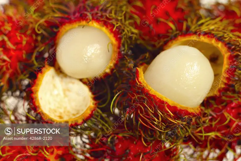 A pile of rambutan fruits with two opened to reveal the delicious interior