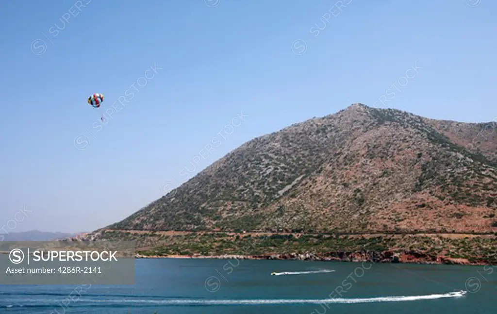 A holidaymaker enjoys a parasailing adventure at Bali, on the north coast of the Greek Island of Crete. The tow-boat is bottom right.