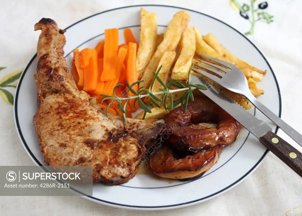 A pork chop cooked in white wine with apple rings, fries and  carrots