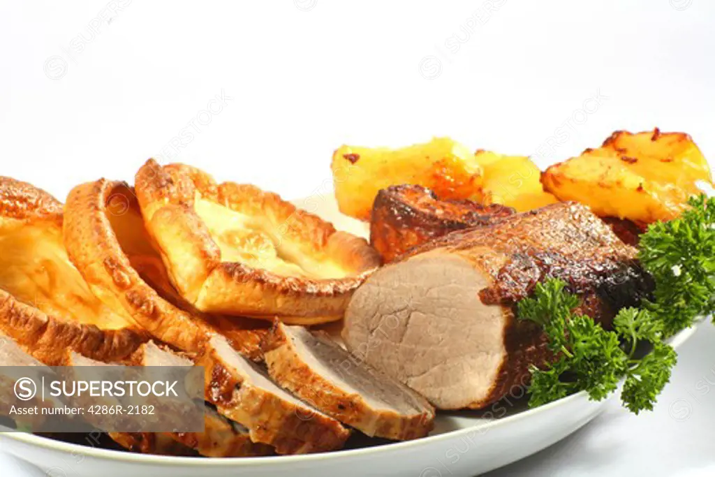 A serving dish of roast beef cut into thick medallions, with yorkshire puddings, roast potatoes and parsley