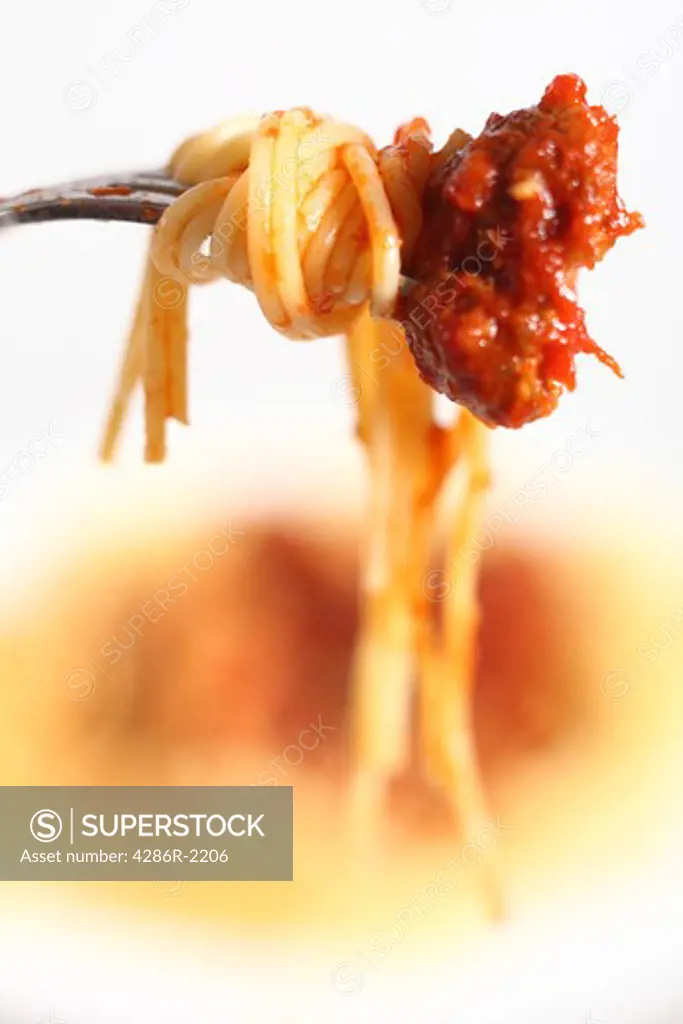 An Italian-style meal of spaghetti and meatballs in tomato sauce, focus on a single meatball on a fork with pasta