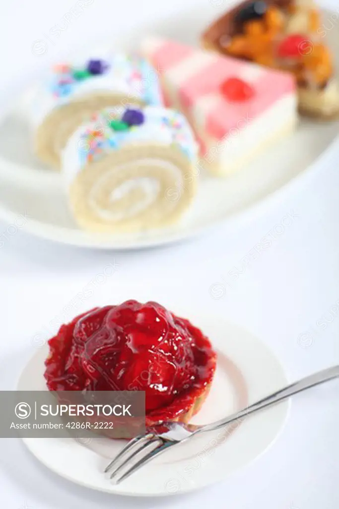 A strawberry tart and fork with a plate of cakes in the background