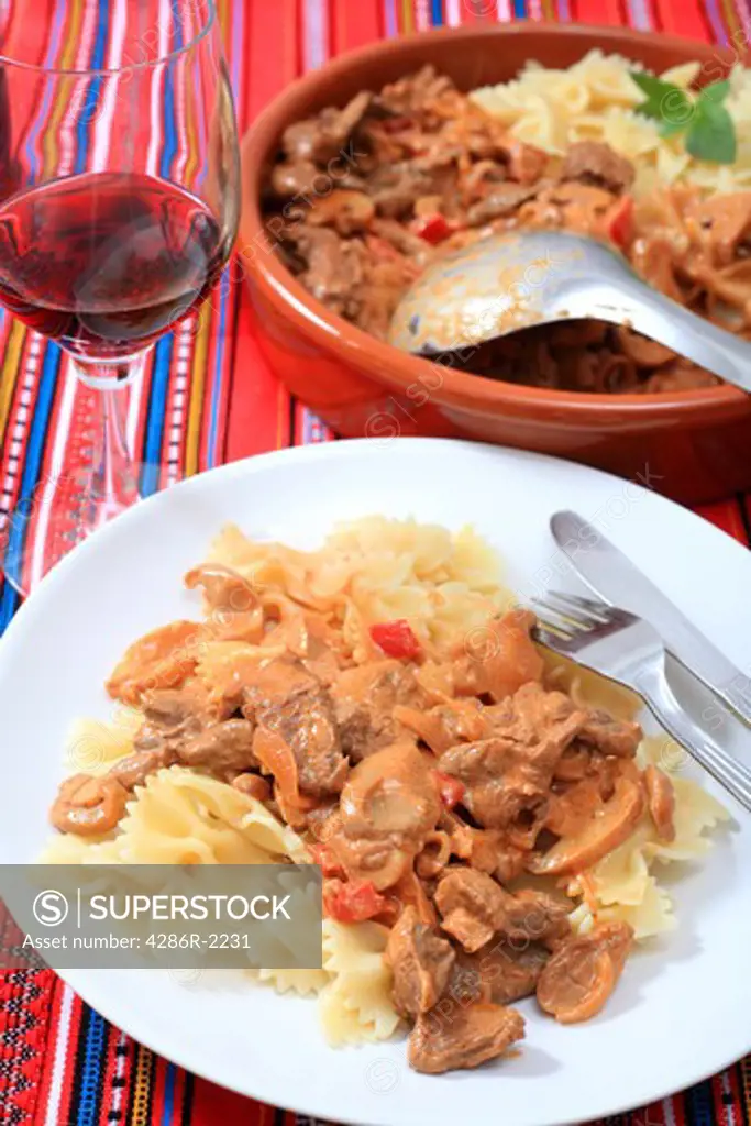 A dinner of beef stroganoff with pasta and wine