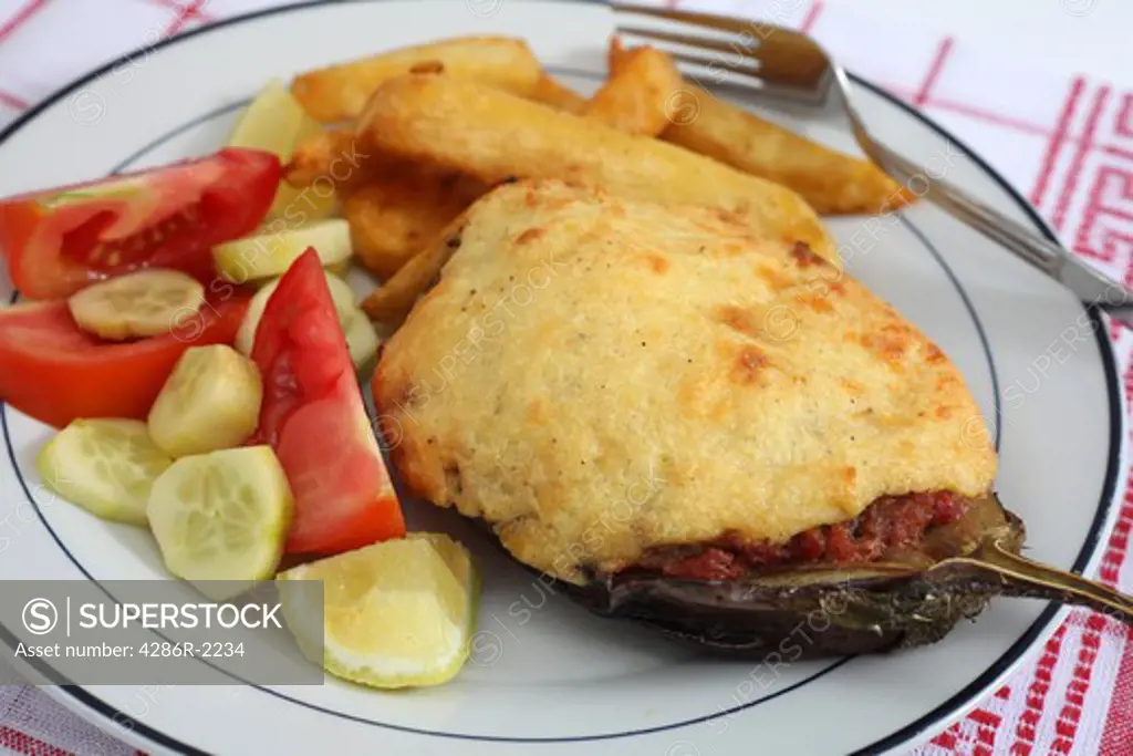Traditional Greek 'papoutsakia', eggplant stuffed with meat, tomato and parsley sauce and topped with bechamel, being served with a tomato and cucumber salad and french fried potato chips.