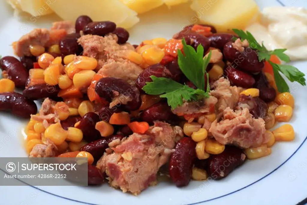 Close-up view of a tuna, kidney bean and sweetcorn salad on a plate with boiled potatoes and mayonnaise