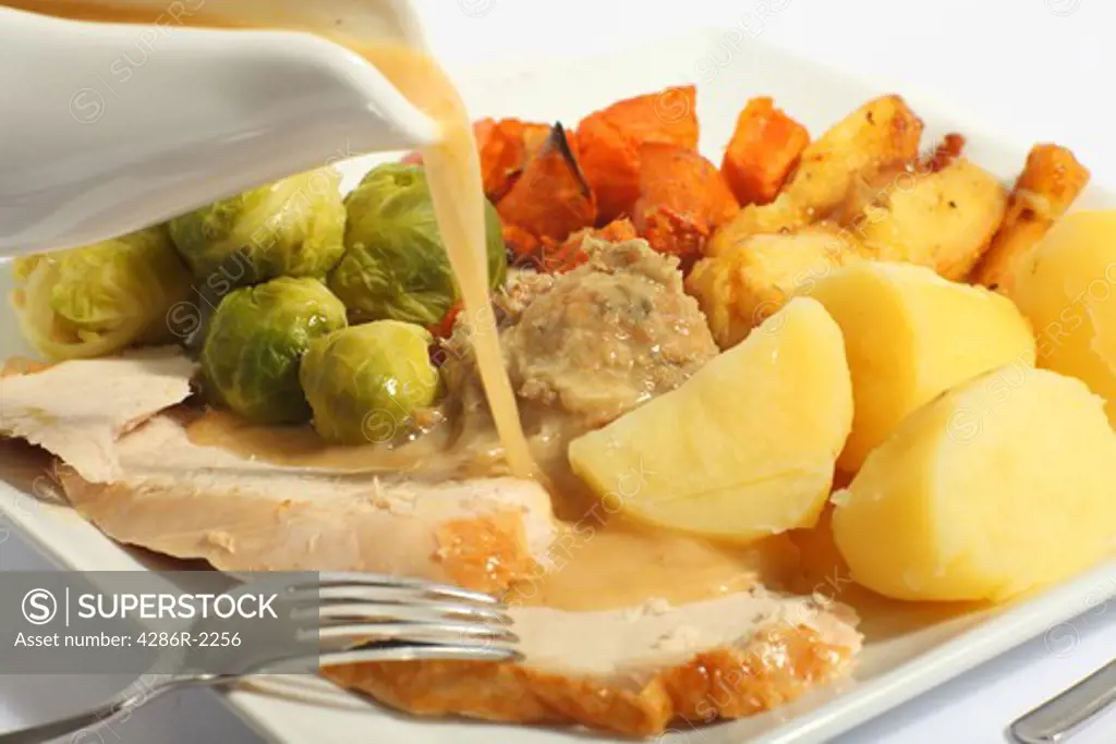 Pouring gravy on a festive turkey meal, with roast yams, roast parsnips, boiled potatoes and stuffing