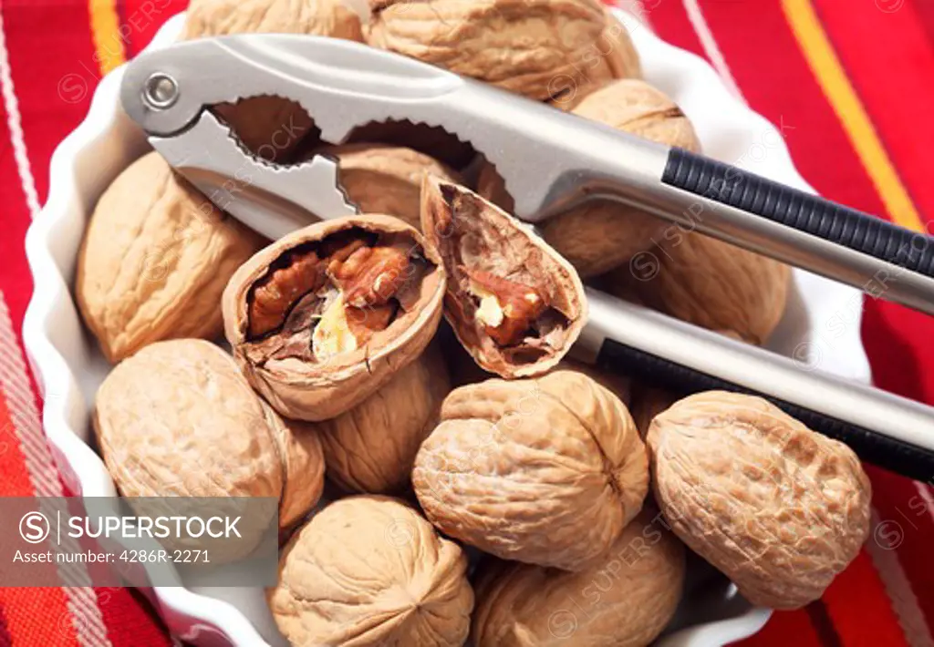 A bowl of walnuts with a pair of nutcrackers, one of the nuts broken open