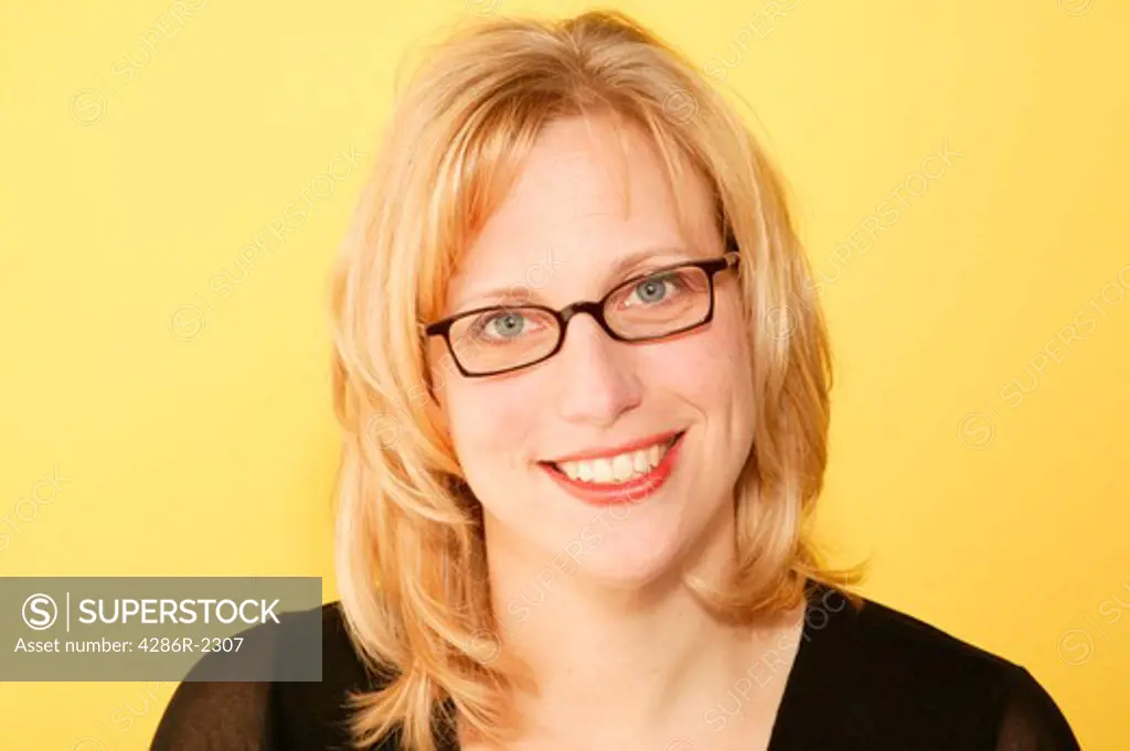 Studio shot of a blonde woman wearing glasses with a bright smile.