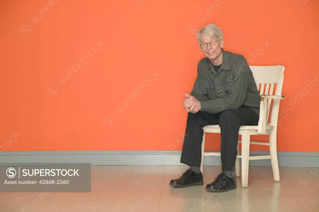 Man smiling  in chair with orange background