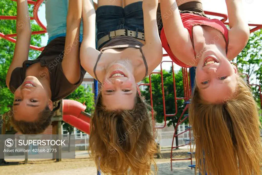 Three young girls hanging upside down in a park and laughing