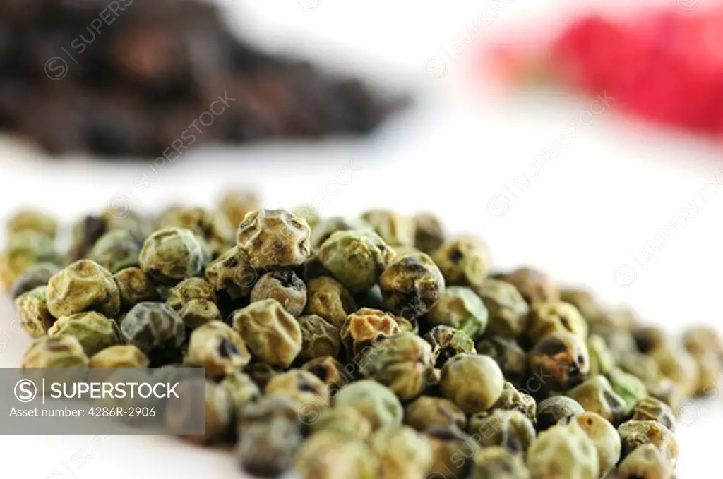 Heaps of green, black and red peppercorns on white background