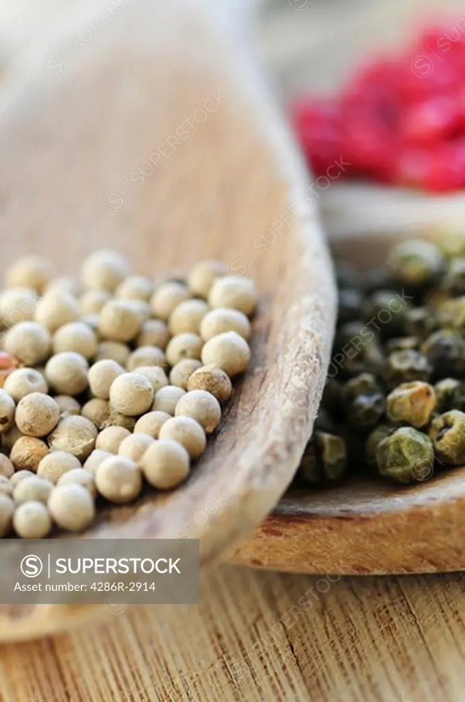 Different kinds of peppercorns in wooden cooking spoons macro