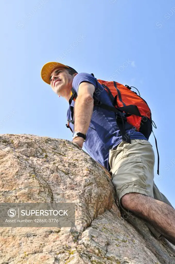 Middle aged man with backpack climbing a rock