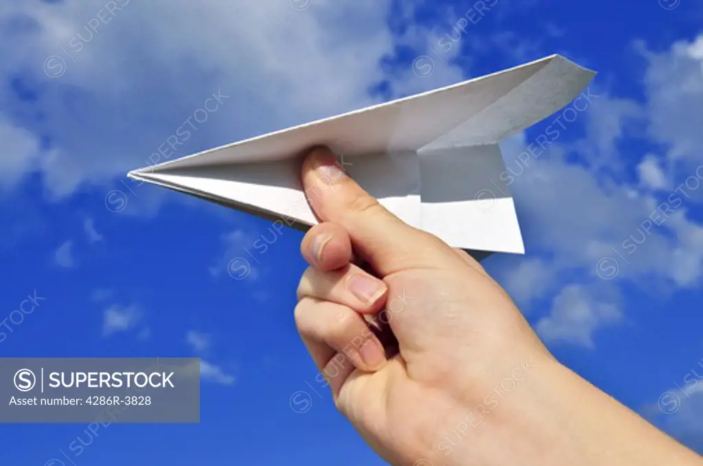 Child's hand holding a paper airplane on blue sky background
