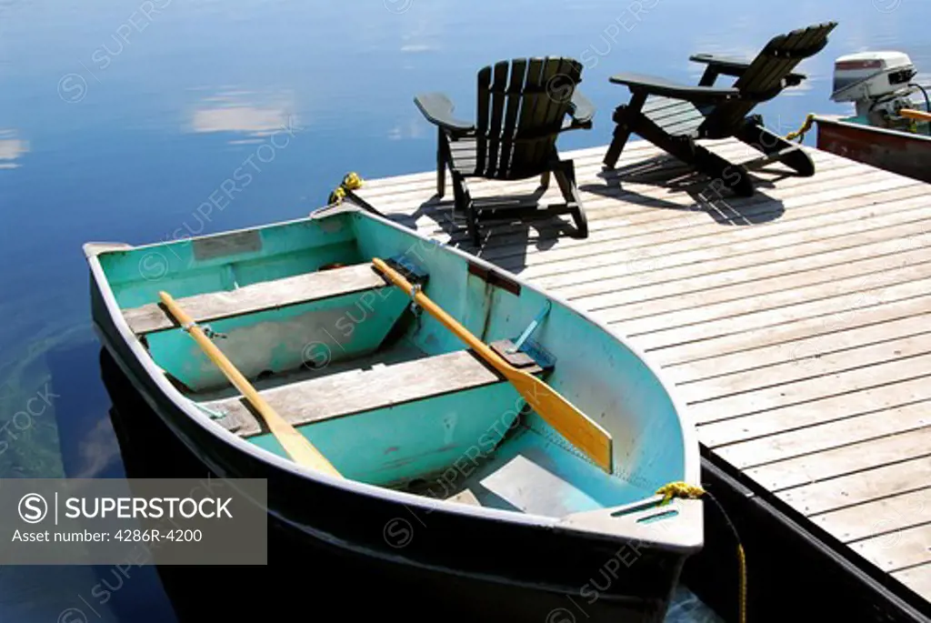 Two wooden adirondack chairs on a boat dock on a beautiful still lake with sky reflection