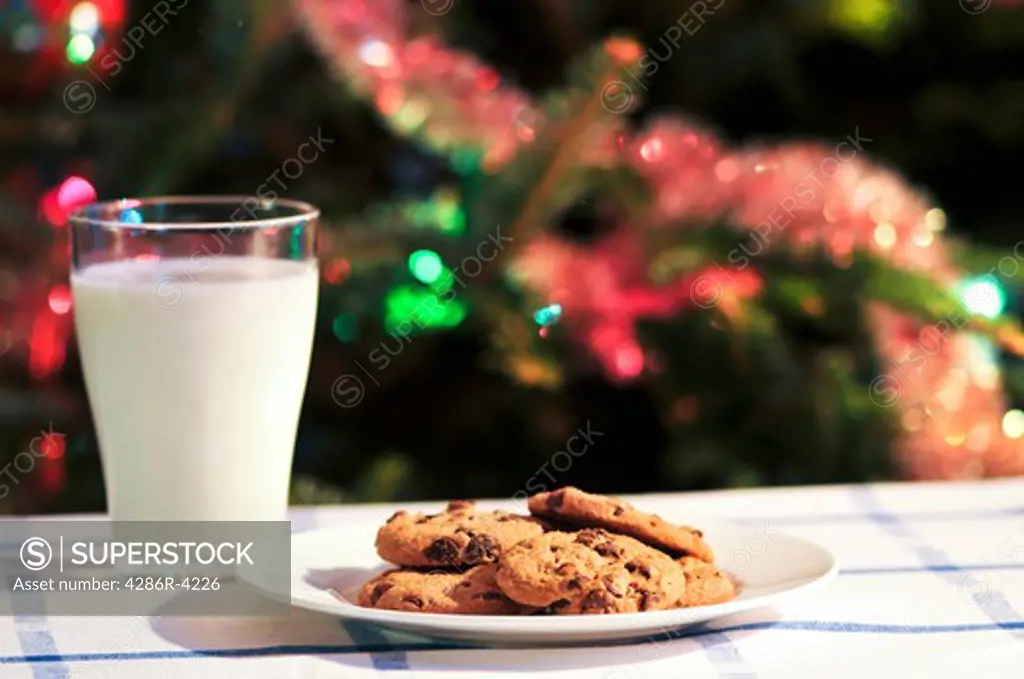 Plate of cookies and glass of milk near Christmas tree