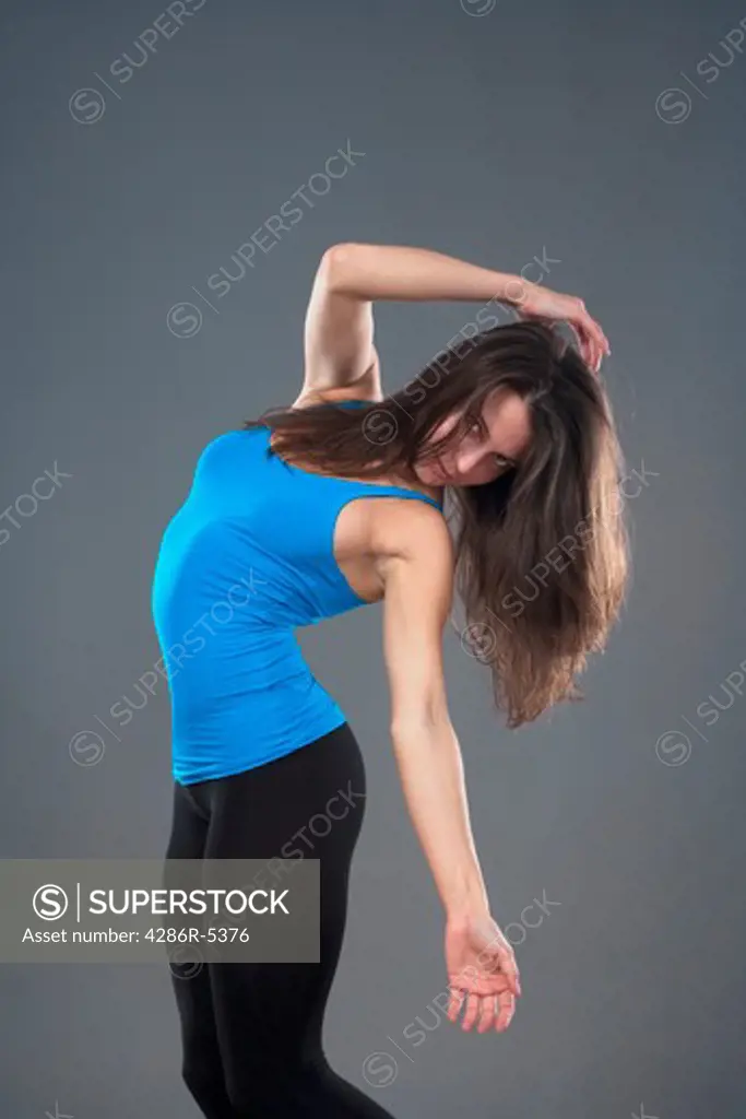 energetic young woman with blue top dancing - isolated on gray background