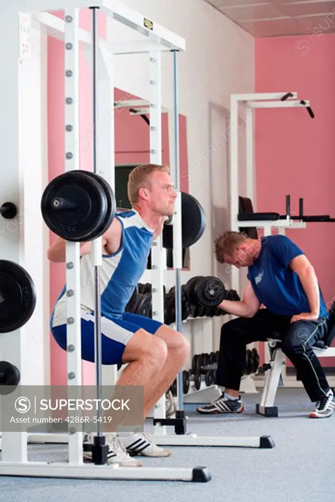 young man lifting heavy bar-bell in modern gym