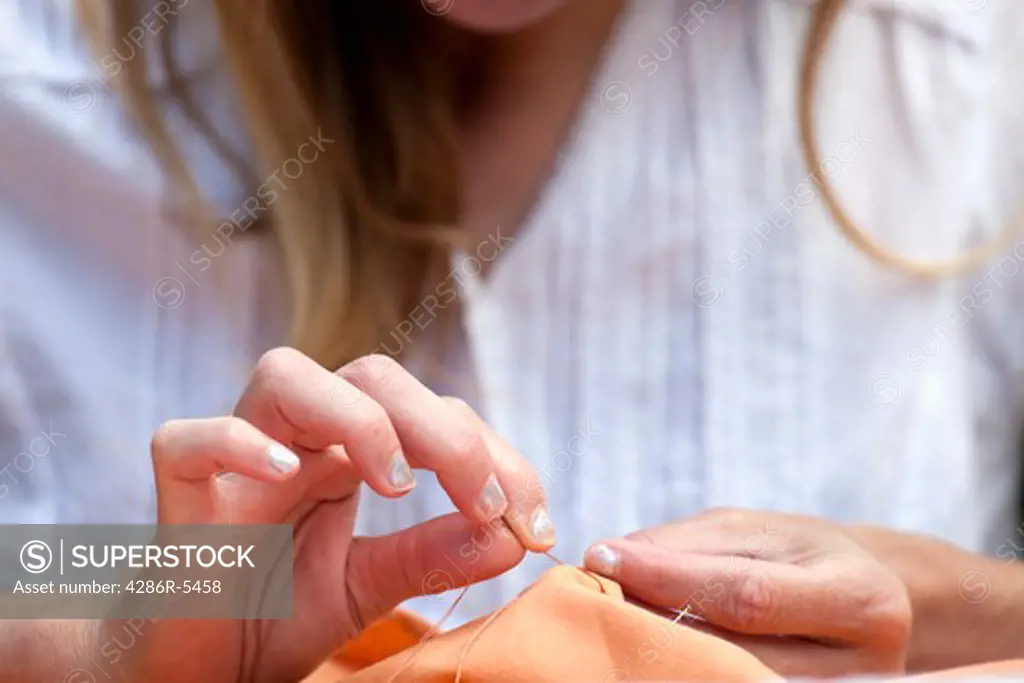 closeup of womans hands sewing orange cloth outdoors