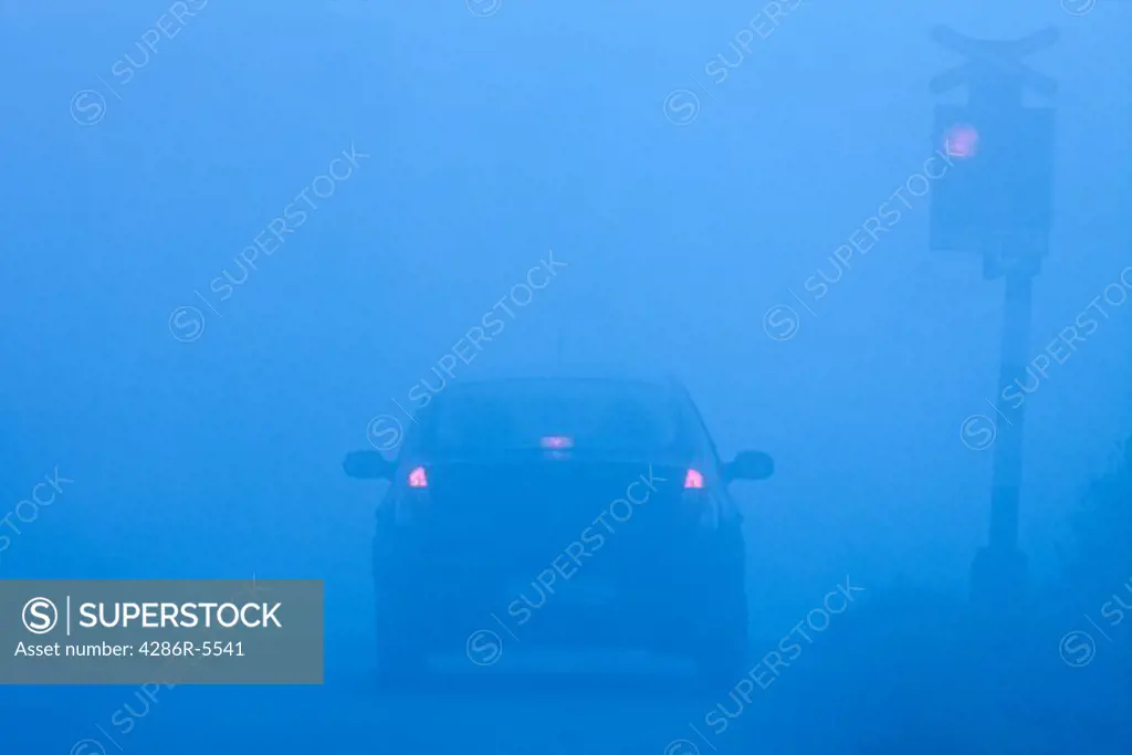 car waiting at rural railroad crossing with red lights blinking in fog