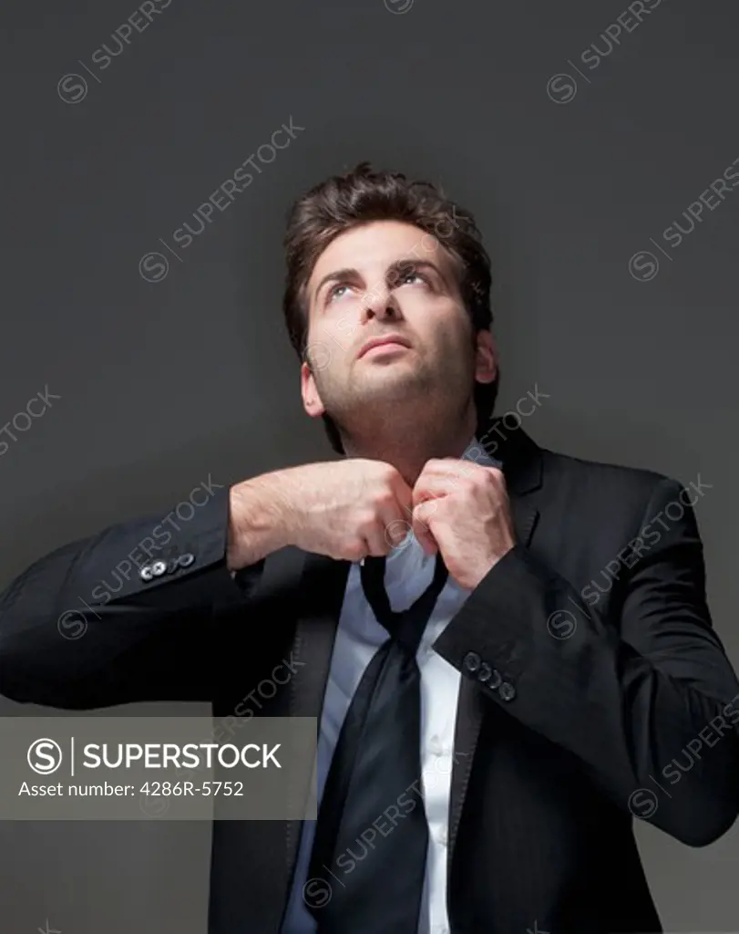 businessman in suit loosening up his tie - isolated on gray