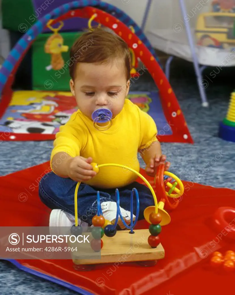 male caucasian toddler sitting on floor playing with toy pacificer in mouth