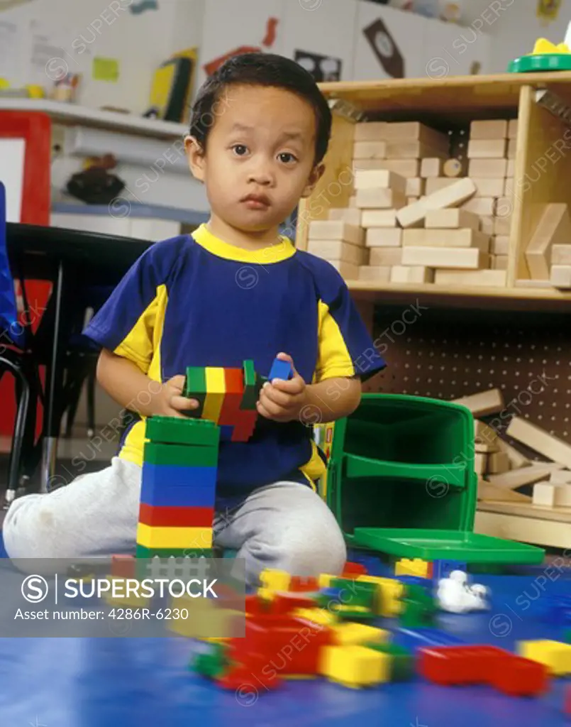 Young asian boy sitting on floor of nursery school playing with bright colored blocks