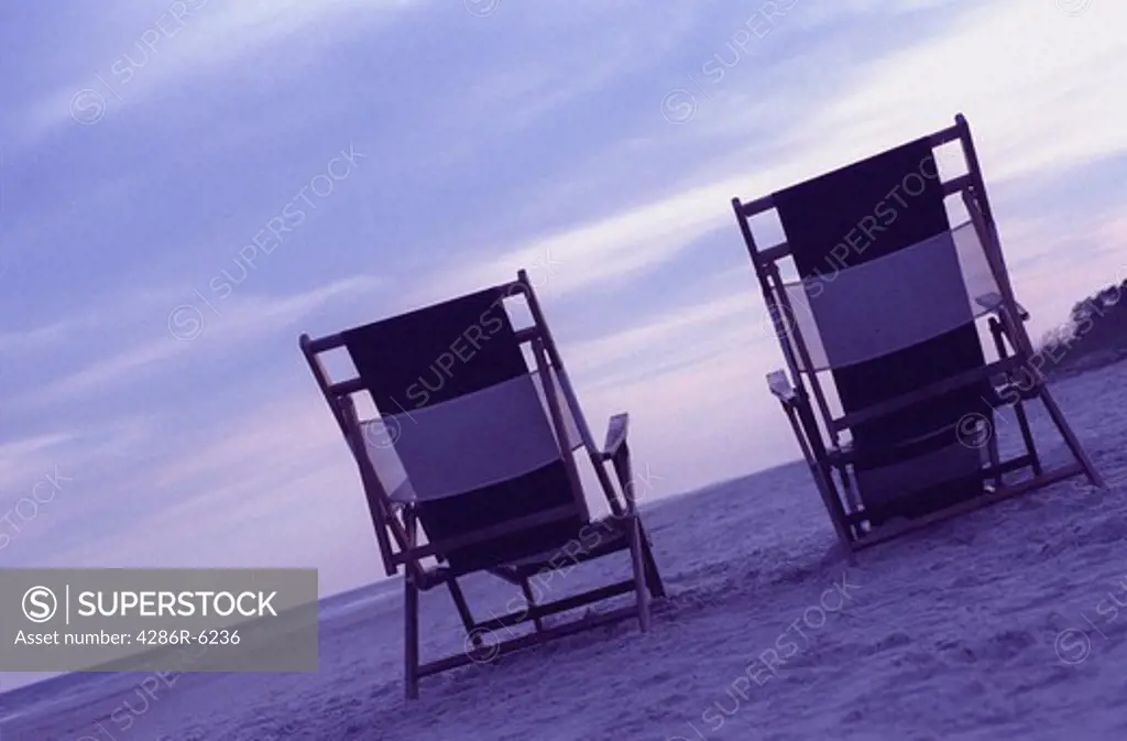 Two empty canvas beach chairs facing the ocean's edge.