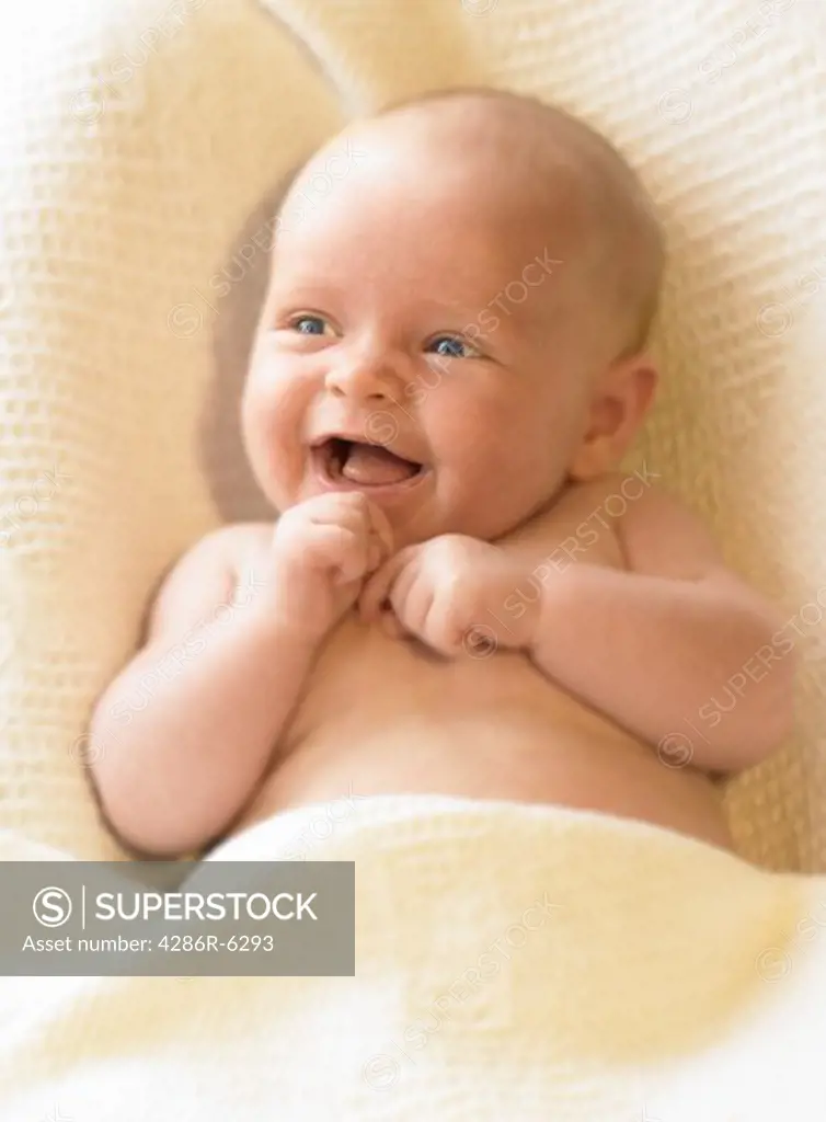 Close up of a young infant smiling and looking toward the left of the frame.